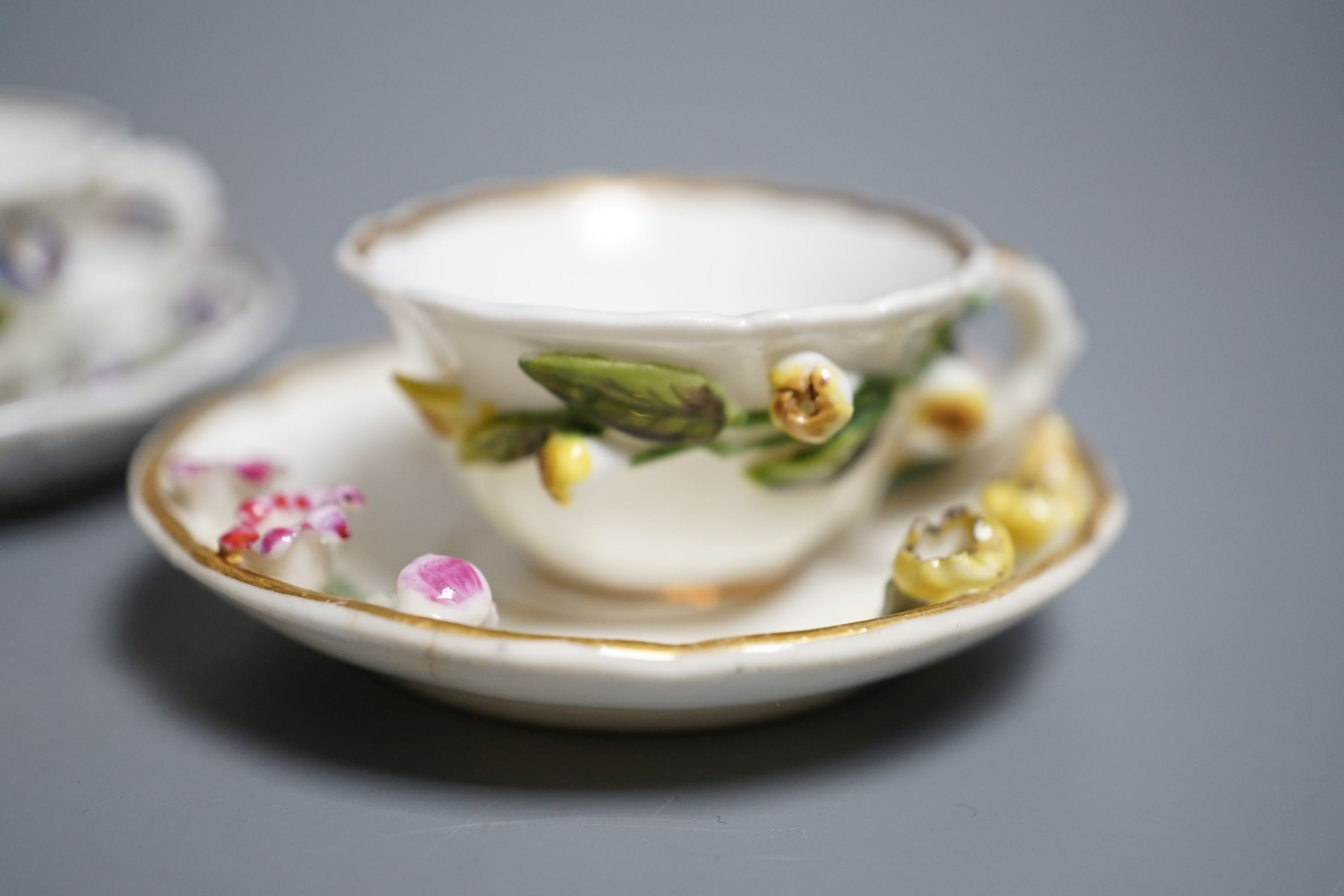 Two Rockingham miniature flower encrusted cups and saucers, c.1830. Provenance - Mona Sattin collection of miniature cups and saucers, collection no. 199 and 200.